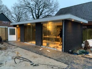 moderne aanbouw met glazen gevels en zwarte gevelbekleding.