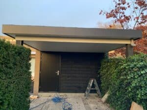 modern tuinhuis met zwarte houten gevel en witte overhang in een tuin met groene en rode beplanting.